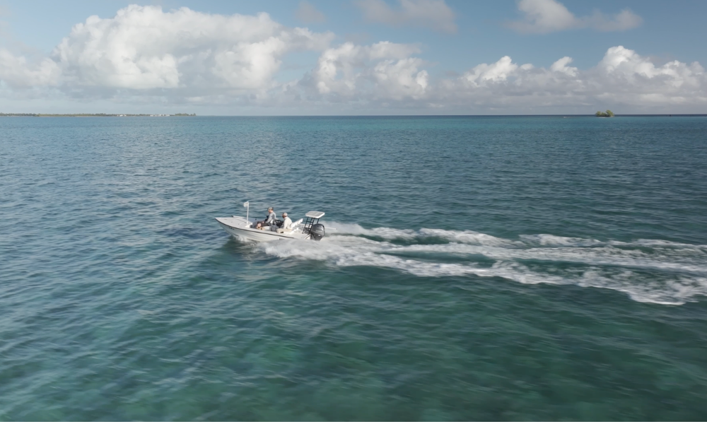 A small motorboat cruises across the clear blue ocean under a partly cloudy sky, leaving a white wake behind. Two guests enjoy a private boating excursion on the open sea near Caerula Mar Club, South Andros Island, The Bahamas.